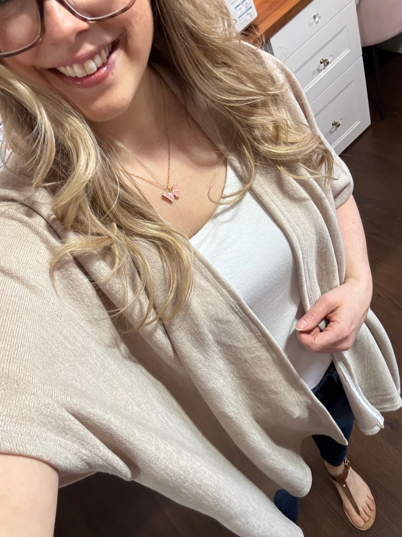 Model wearing a beige kimono cardigan over a white tank top and jeans, standing in a stylish home studio