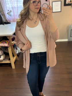 Smiling woman taking a mirror selfie while wearing a pink City Shrug over a white tank top and dark jeans, paired with casual sandals.