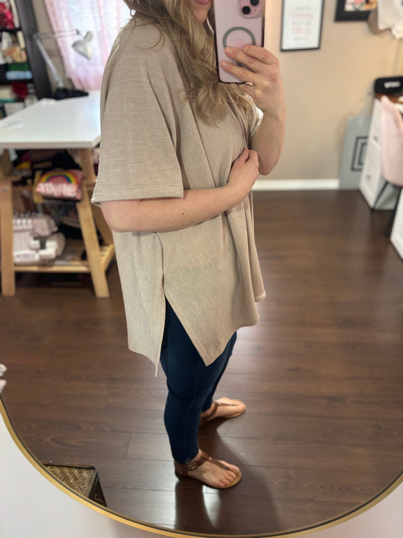 Model wearing a beige kimono cardigan over a white tank top and jeans, standing in a stylish home studio