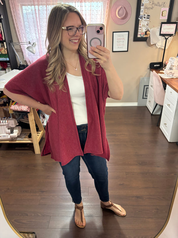 Model wearing a red/pink kimono cardigan over a white tank top and jeans, standing in a stylish home studio