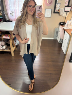 Model wearing a beige kimono cardigan over a white tank top and jeans, standing in a stylish home studio