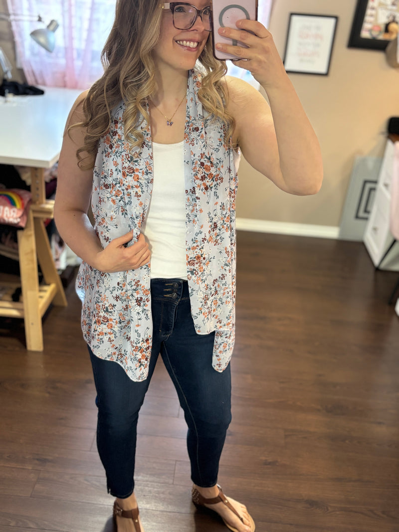 Woman wearing a lightweight blue floral vest over a white tank top and jeans, showcasing a stylish and versatile layering piece