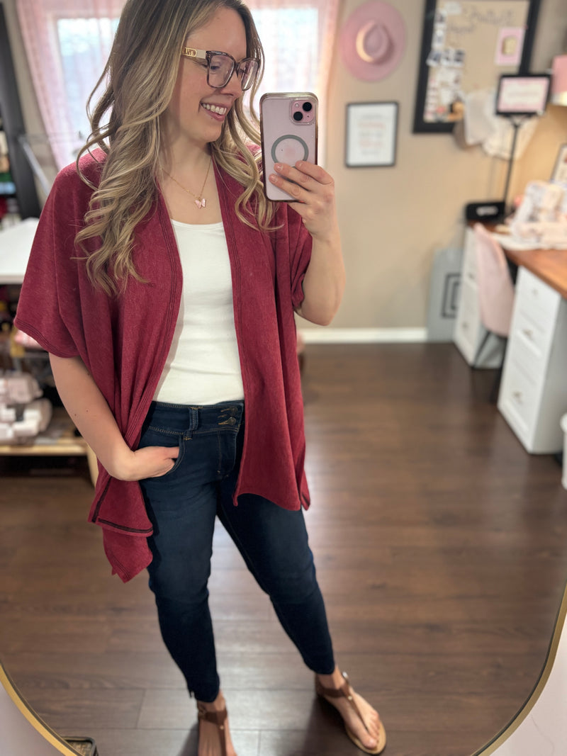 Model wearing a red/pink kimono cardigan over a white tank top and jeans, standing in a stylish home studio