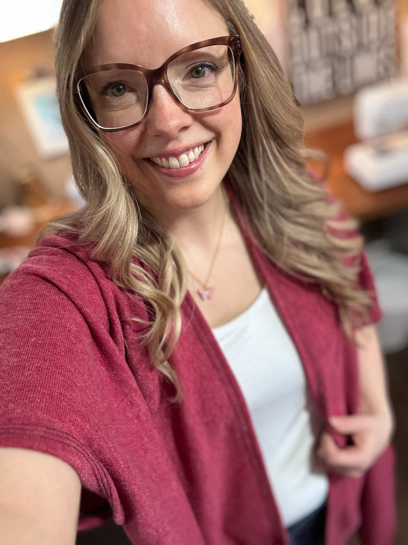 Model wearing a red/pink kimono cardigan over a white tank top and jeans, standing in a stylish home studio