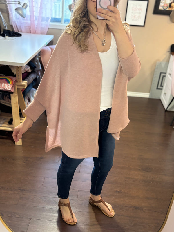 Smiling woman taking a mirror selfie while wearing a pink City Shrug over a white tank top and dark jeans, paired with casual sandals.